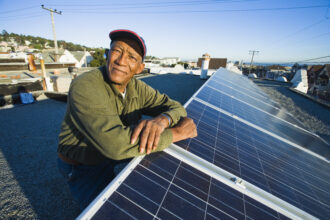 Lawrence Jackson of San Francisco is pictured with the rooftop solar system he had installed by GRID Alternatives.