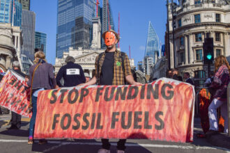 A protester wearing a mask holds an anti-fossil fuels banner during the demonstration outside the Bank of England. Credit: Vuk Valcic/SOPA Images/LightRocket via Getty Images