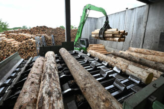 An excavator loads logs used for wood pellets at a sawmill.