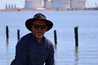 John Beard Jr., the founder and executive director of the Port Arthur Community Action Network, stands in front of the ExxonMobil and QatarEnergy’s Golden Pass LNG facility, just south of Port Arthur, Texas. Beard is a retired refinery worker who first challenged the Port Arthur LNG emissions permit. Credit: James Bruggers/Inside Climate News