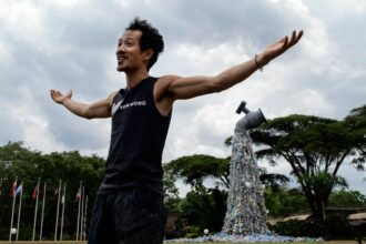 Canadian activist and artist, Benjamin von Wong is pictured in front of his 30-foot monument themed 'turn off the plastics tap' created using plastic waste from Nairobi's largest slum, Kibera, standing outside the venue of the Fifth Session of the United Nations Environment Assembly, at the United Nations Environment Programme (UNEP) Headquarters in Nairobi on Feb. 22, 2022. Credit: Tony Karumba/AFP via Getty Images