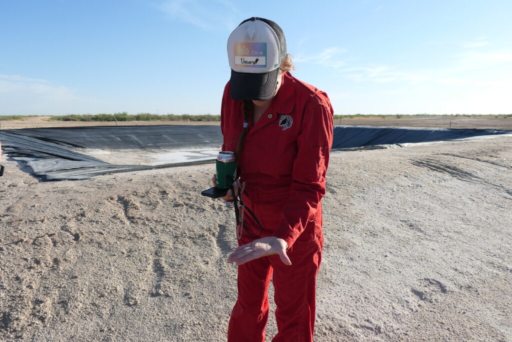 Oil and gas lawyer Sarah Stogner picks up a salt crystal left over from produced water that spewed from a geyser at an orphaned well. The remediation site in Crane County shows the devastating impacts of produced water on the land. Credit: Martha Pskowski/Inside Climate News