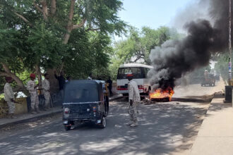 Sudanese security forces intervene in October 2021 as smoke billows from tyres set on fire by Sudanese students in the city of Nyala, the capital of South Darfur, demonstrating against the hikes in bread prices due to low wheat supply following the closure of Sudans' Red Sea port of Port Sudan. Credit: Abdelmonim Madibu/AFP via Getty Images.