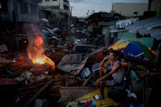 A resident sits in front of his destroyed house as another makes a fire in a devastated area in the aftermath of Typhoon Haiyan on Nov. 17, 2013 in Tacloban, Philippines. Credit: Kevin Frayer/Getty Images